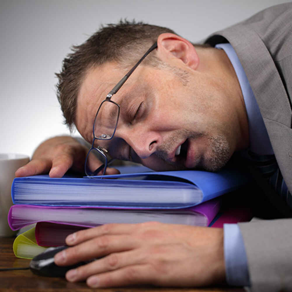 Man sleeping on folders on desk due to experiencing sleep apnea fatigue and tiredness