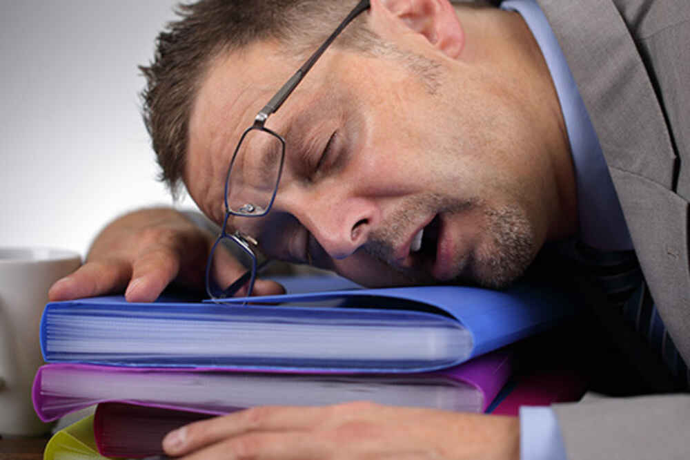 Man sleeping on folders on desk due to experiencing sleep apnea fatigue and tiredness